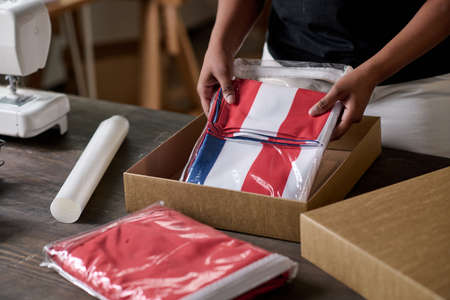 Hands of young black woman putting folded handmade USA flag into box while packing it to send to American veterans of laborの写真素材