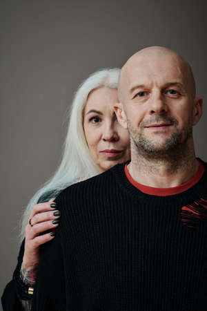 Vertical medium close-up studio portrait of mature man and woman in love posing on camera, gray...