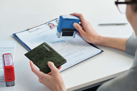 Unrecognizable woman working in embassy office giving approval to visa application putting stamp on...