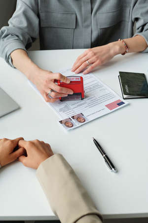 Vertical high angle view in unrecognizable US embassy worker putting rejected stamp on visa...