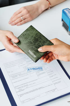 Vertical high angle of unrecognizable woman giving her passport to consular officer to make travel...