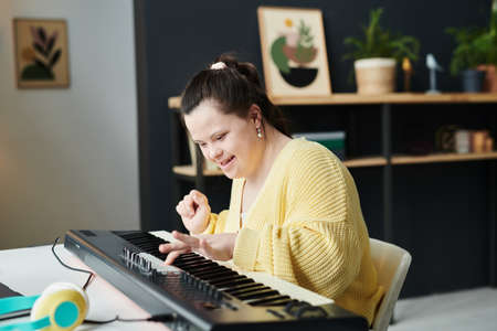 Portrait of young Caucasian woman with Down syndrome spending time at home having fun playing electronic keyboardの写真素材