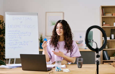 Young female influencer sitting in front of laptop speaking about periods and menstrual cups