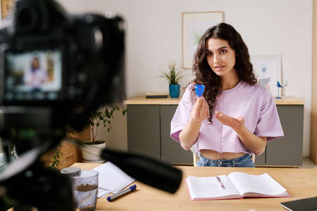 Young woman with long curly hair sitting at desk in front of camera speaking about experience of...