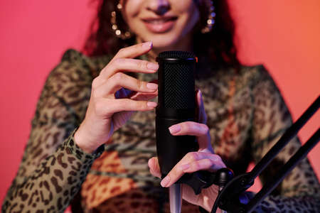 Selective focus of young female blogger sitting in studio in pink and yellow neon light recording...