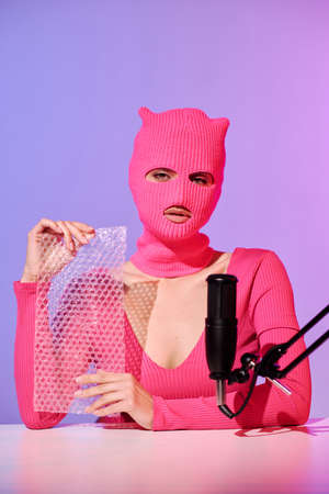 Unrecognizable young female influencer wearing pink sweater and balaclava holding bubble plastic wrap prepared for ASMR contentの写真素材