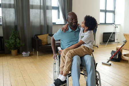 African disabled father sitting in wheelchair with little son on his knees and talking to himの写真素材