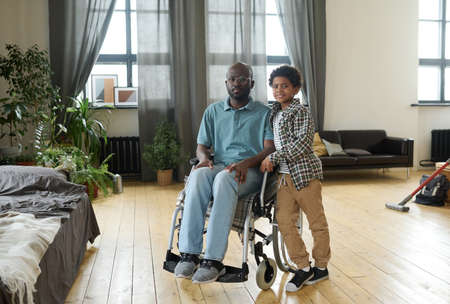 Portrait of African disabled father sitting in wheelchair and looking at camera together with his littlesonの写真素材