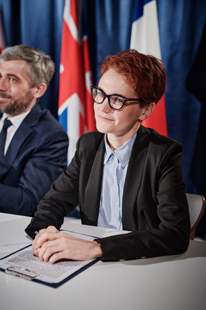 Young speaker in eyeglasses sitting at table with report during political debate