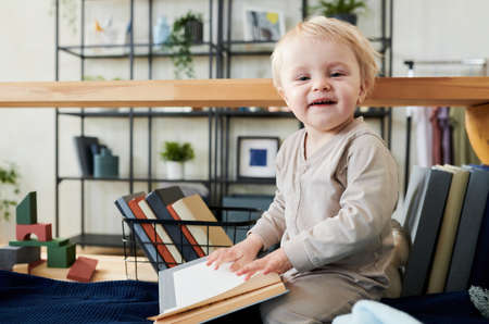 Portrait of adorable child looking at camera while sitting on bed and flipping through the pages of...