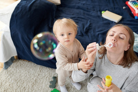 High angle view of young mother blowing bubbles up in the air with her little son watching for them