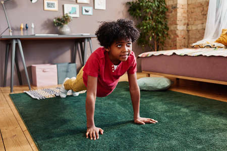 African little boy watching sport program and repeating physical exercises on the floor in his roomの写真素材