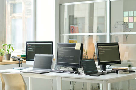 Horizontal image of workplace of IT specialist with codes on screens of computers and laptops on...