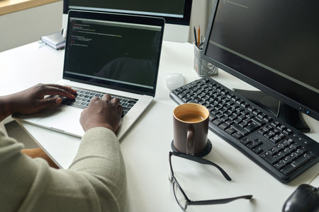 Close-up of programmer sitting at his workplace with cup of coffee and writing codes on laptopの写真素材