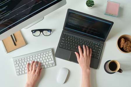 High angle view of young programmer writing code on laptop and using computer keyboard at table