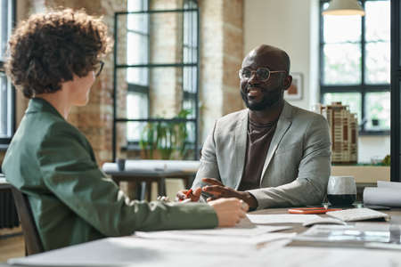 African customer discussing project together with architect at table during their meeting at officeの写真素材