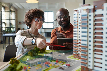 Two architects discussing construction mock-up of building together during teamwork at office