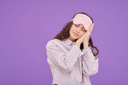 Portrait of young woman in sleep mask closed her eyes and putting head on her hands during dreaming...