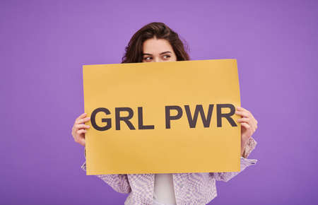 Portrait of young girl standing behind Girl Power poster against purple background and supporting women rightsの写真素材
