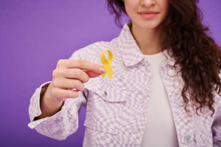 Close-up of young woman holding yellow ribbon in front of her on color background