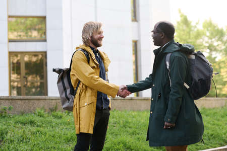 Two multiethnic colleagues greeting each other and smiling during meeting outdoors in the cityの写真素材
