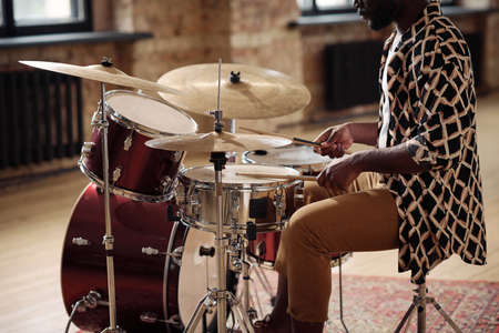 African musician playing at drums set with drumsticks at empty studioの写真素材