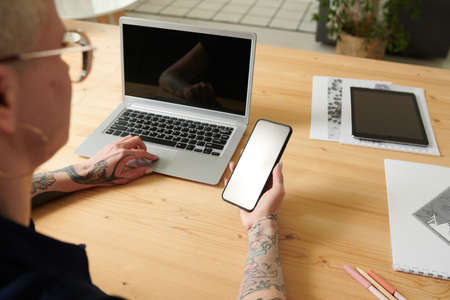 Close-up of woman reading a message on her smartphone while working on laptop at her workplace