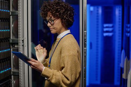 Female engineer opening server rack and checking the work of computer network with digital tablet