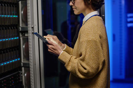Young female engineer checking data on digital tablet while working with supercomputer in data...