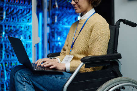 Close-up of female engineer with disability sitting in wheelchair and typing on laptop, she managing...