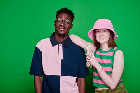 Portrait of stylish multiethnic teenage couple in fashion clothes smiling at camera posing against green backgroundの写真素材