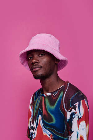 Portrait of African teenage boy in panama hat and bright shirt posing against pink backgroundの写真素材
