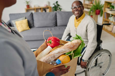 Close-up of caregiver holding paper bag with food bringing home for man with disabilityの写真素材