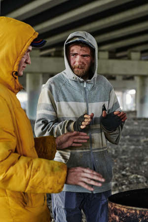 Homeless people warming up in front of drum fire outdoors under the bridgeの写真素材