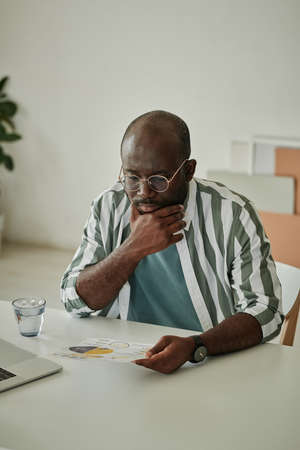 African businessman sitting at his workplace at office and examining document with chartの写真素材