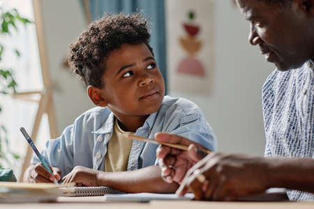 African schoolboy listening to his teacher explaining new topic at table during home schoolingの写真素材