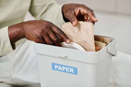 Close-up of African man separating paper in special container for recycling