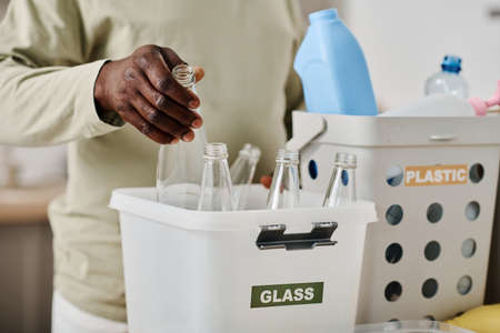 Close-up of African man separating glass bottles in container for recycling at homeの写真素材