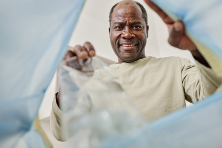 Low angle view of smiling African man throwing plastic bottle in trash binの写真素材