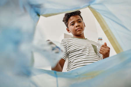 Low angle view of African boy throwing plastic bottles in trash binの写真素材