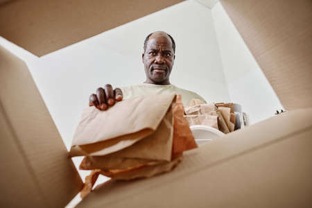 Low angle view of African man throwing paper in cardboard box for recyclingの写真素材