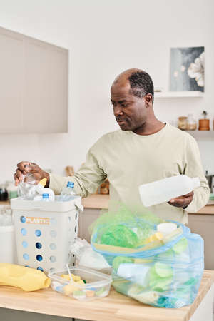 African man separating garbage in different containers at table in the kitchenの写真素材