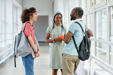 Group of teenagers talking to each other during break standing at corridor after lessonsの写真素材