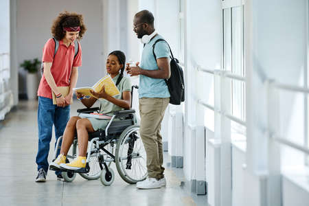 African girl with disability opening textbook and discussing it with her classmates while they standing at corridor after lessonの写真素材