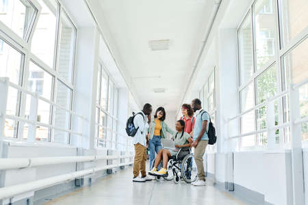 Group of students using laptop together during break while standing at school corridorの写真素材