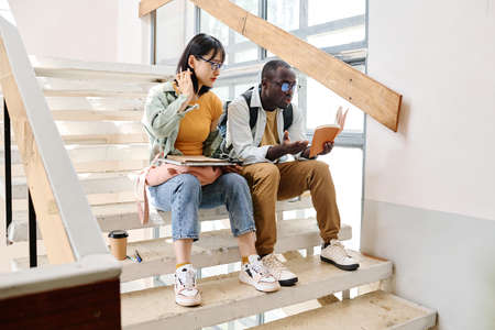 Couple of friends sitting on stairs during break and preparing for the exam togetherの写真素材