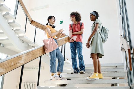 Group of teenagers talking to each other after lessons while standing on stairs of school buildingの写真素材