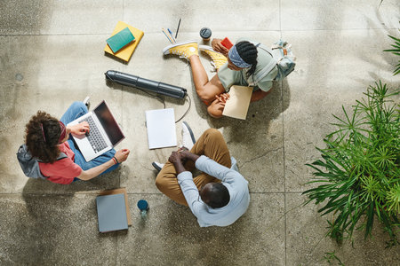 High angle view of college students preparing for the exams together with laptop and textbooks sitting on floor at school corridorの写真素材