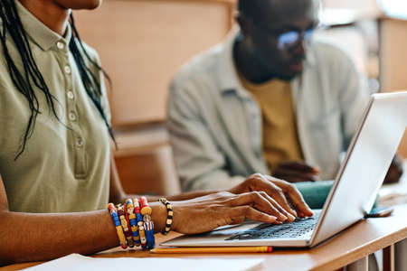 Close-up of African teenage girl typing on laptop at desk during lecture at classroomの写真素材