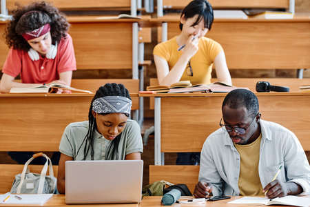 Group of students sitting at desks and writing exam at auditorium of universityの写真素材